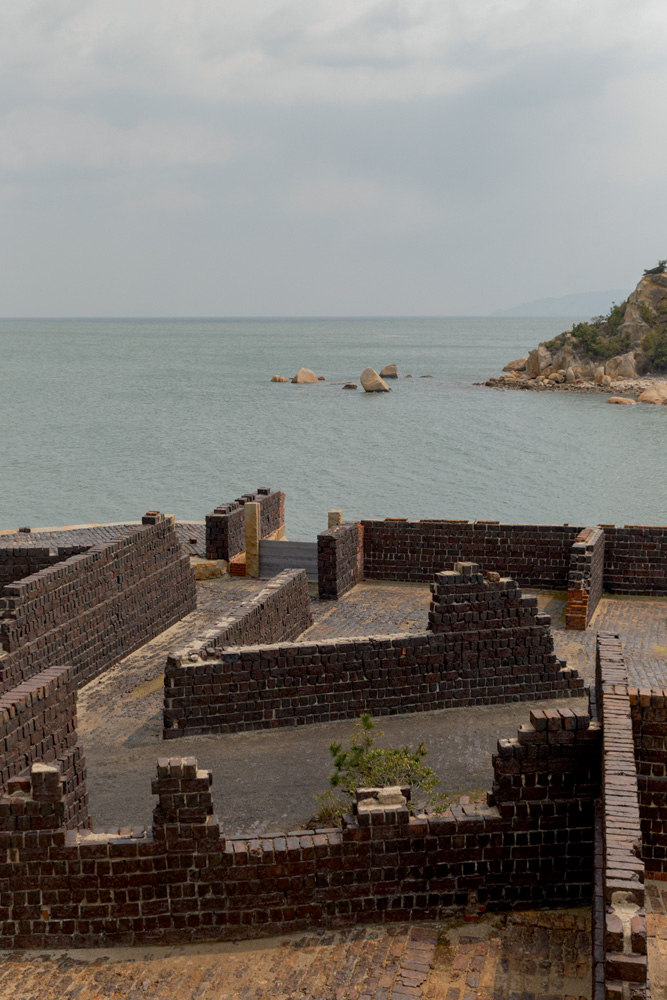 A imagem mostra partes de paredes, ou seja ruínas, em frente ao mar.