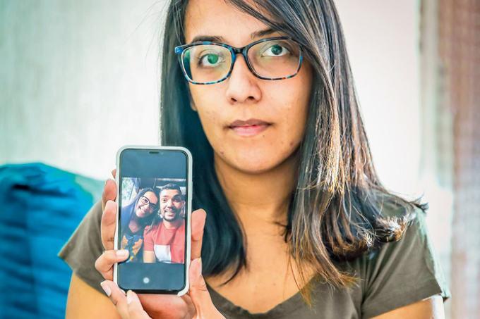 Uma mulher mostrando, pelo celular, uma foto dela com seu ex-noivo para a câmera.