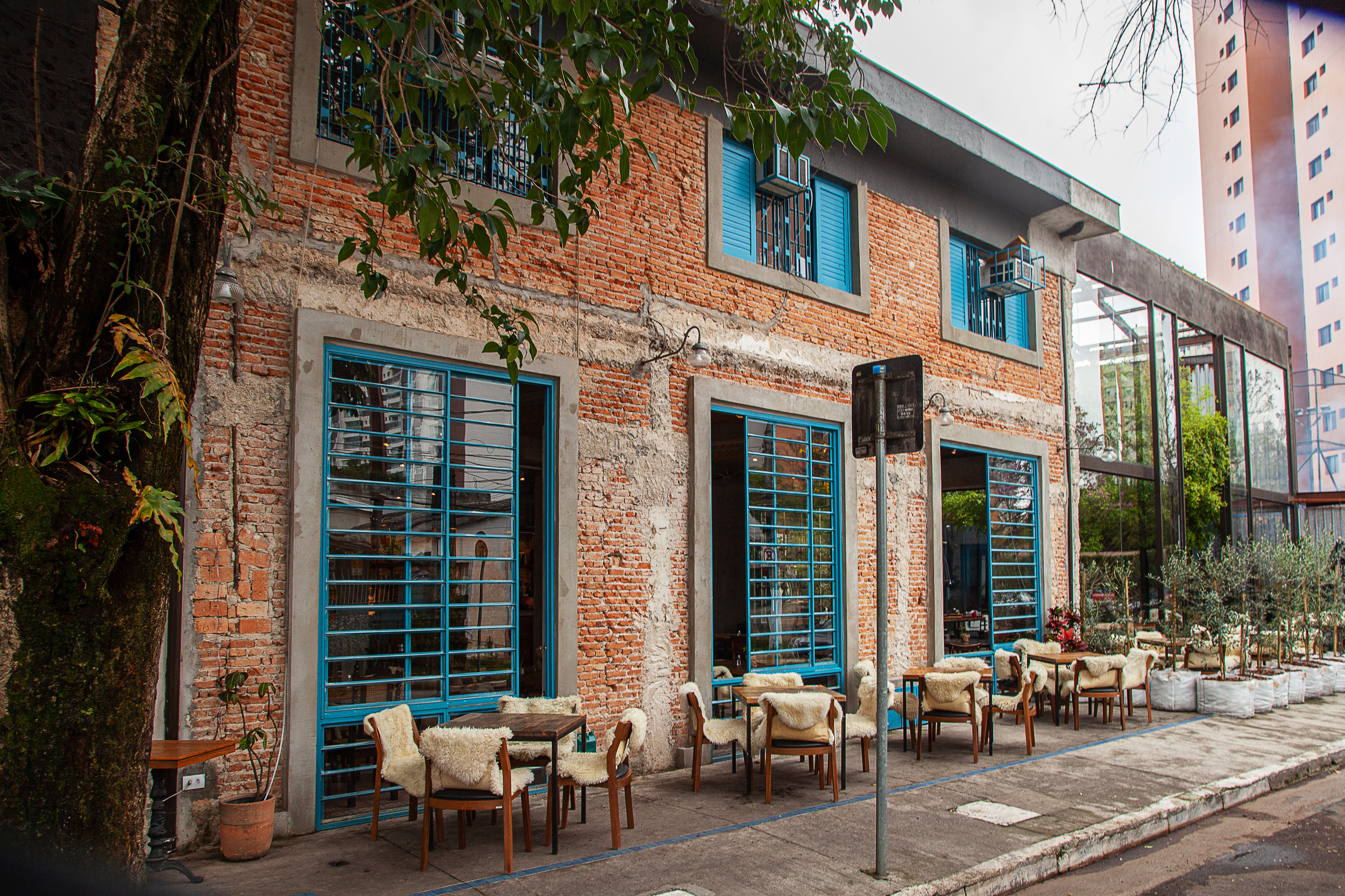 Fachada do bar Quintana com paredes de tijolinhos e mesas na calçada com cadeiras cobertas por cobertores de pelo.