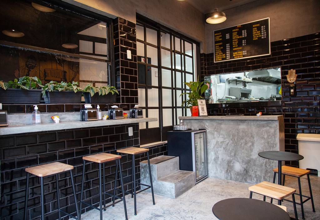 Achados ELO – Nosh Salão da lanchonete Nosh, com banquetas e parede de azulejos pretos à esquerda