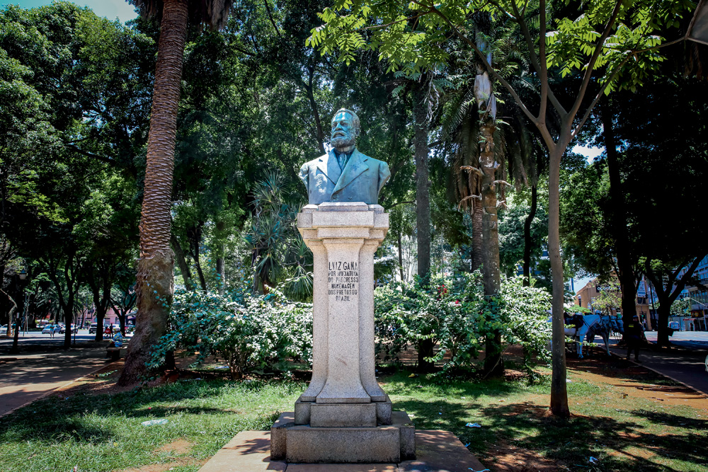 A imagem mostra o Busto de Luiz Gama entre árvores de um parque.