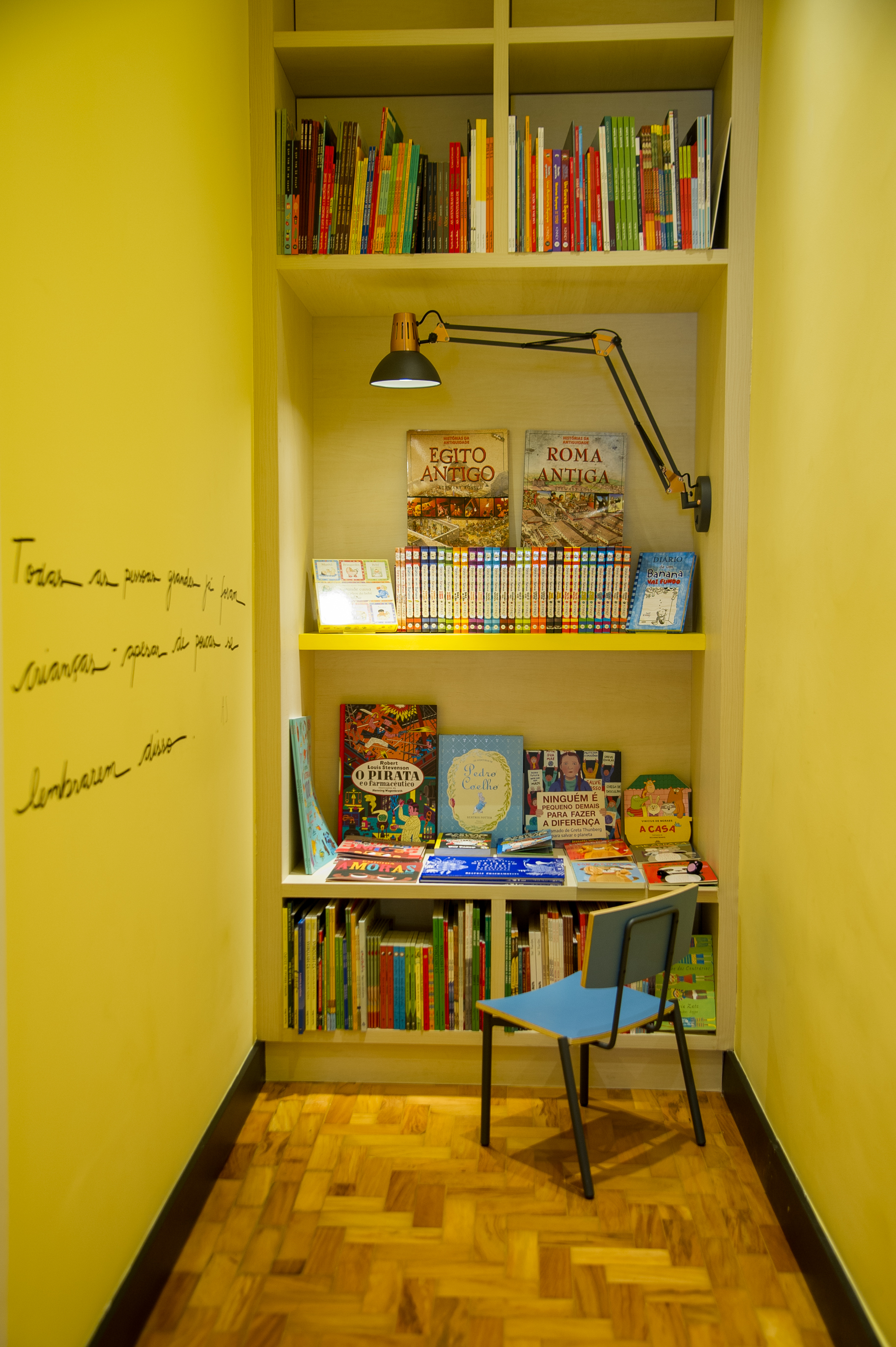 Pequeno vão reúne uma cadeira infantil e livros coloridos no fundo.