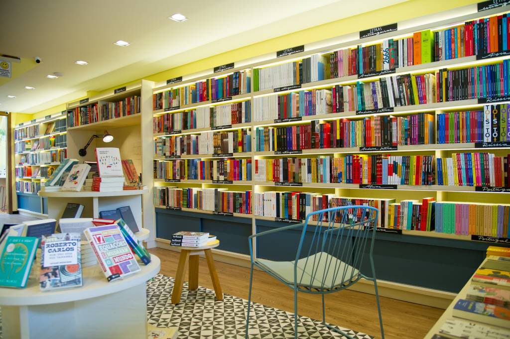 Livraria do Brooklin (Rogério Pallatta) Foto exibe duas cadeiras, tapete, prateleira central com livros e uma grande estante com obras diversas.