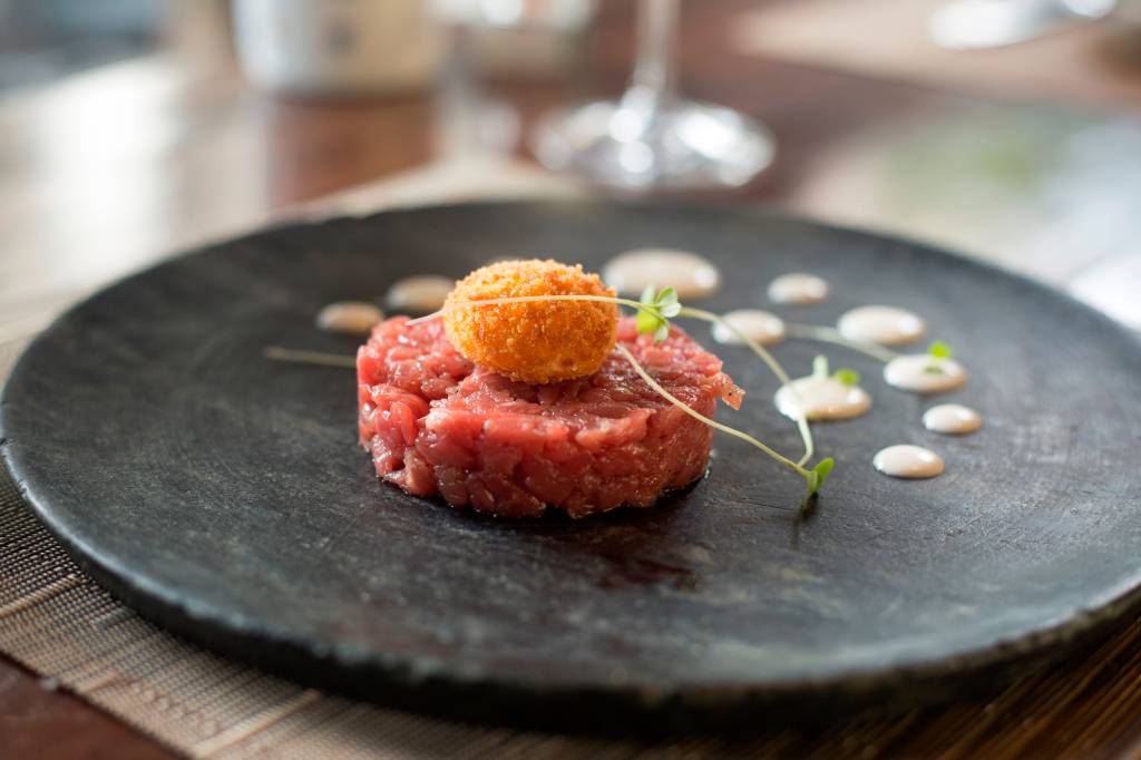 Tartare de carne sobre prato de pedra cinza com gema de ovo frito por cima,