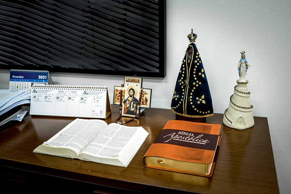 Uma mesa mostra duas bíblias e estátua de Nossa Senhora Aparecida e imagens de Jesus Cristo