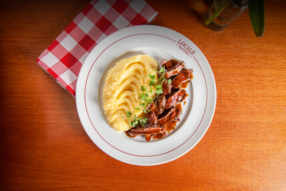 Foto aérea de prato com polenta ao lado de tagliata com molho.