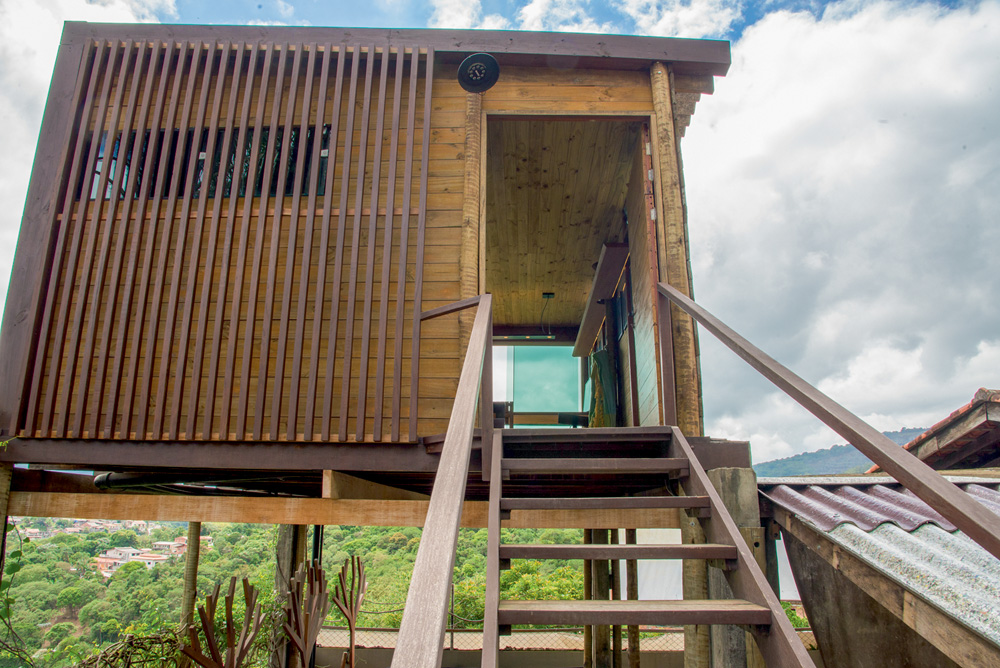 A imagem mostra a entrada de uma cabana, feita de madeira. Tem uma pequena escada, de madeira, na entrada.
