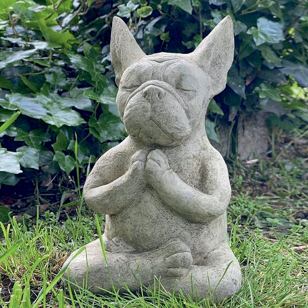Em um jardim, há uma escultura de um buldogue com as mãos paralelas em frente ao peito