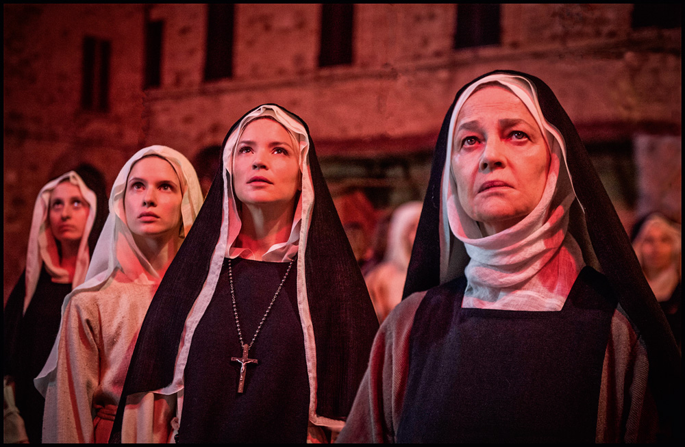 A imagem mostra quatro freiras, em uma luz vermelha, olhando para cima.
