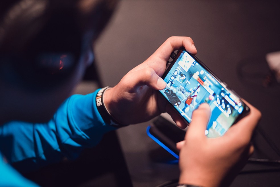 Imagem mostra pessoa segurando celular horizontalmente, com jogo de tiro na tela