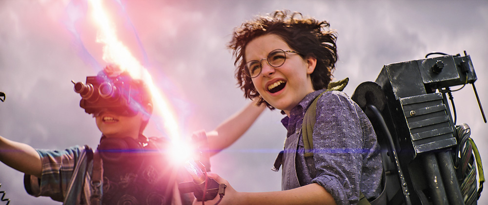 A imagem mostra dois jovens dos novos Ghostbusters usando uma arma que sai um laser dela.