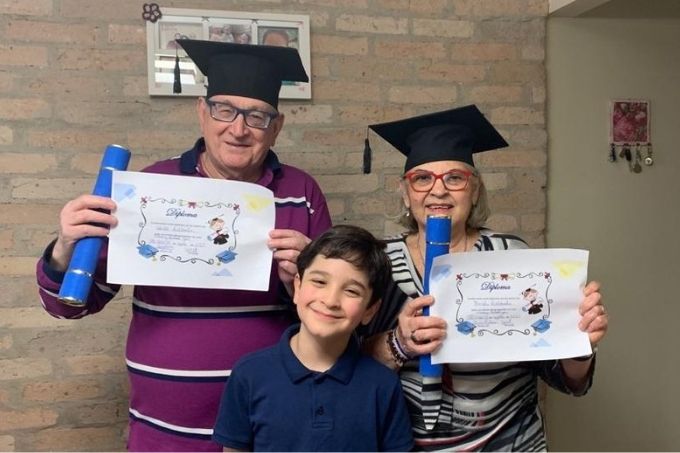 gustavo saldanha sorrindo junto de sua mãe e seu pai, que estão segurando diplomas que o menino ganhou