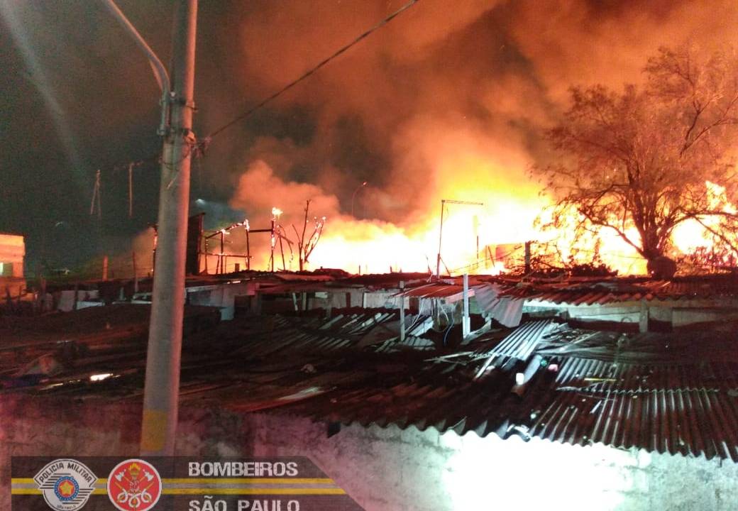 Imagem mostra área de favela com fogo e fumaça ao fundo