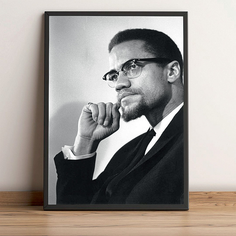 malcolm x.jpg A foto mostra um quadro apoiado na parede e no chão. No quadro, uma foto em preto e branco de Malcolm X olhando para o lado e com a mão no queixo