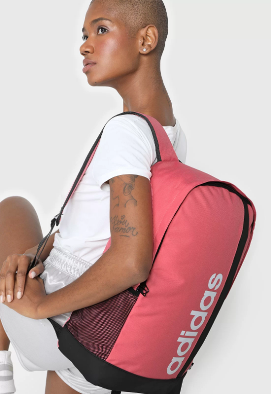 Uma mulher negra está meio de costas segurando uma mochila rosa nas costas