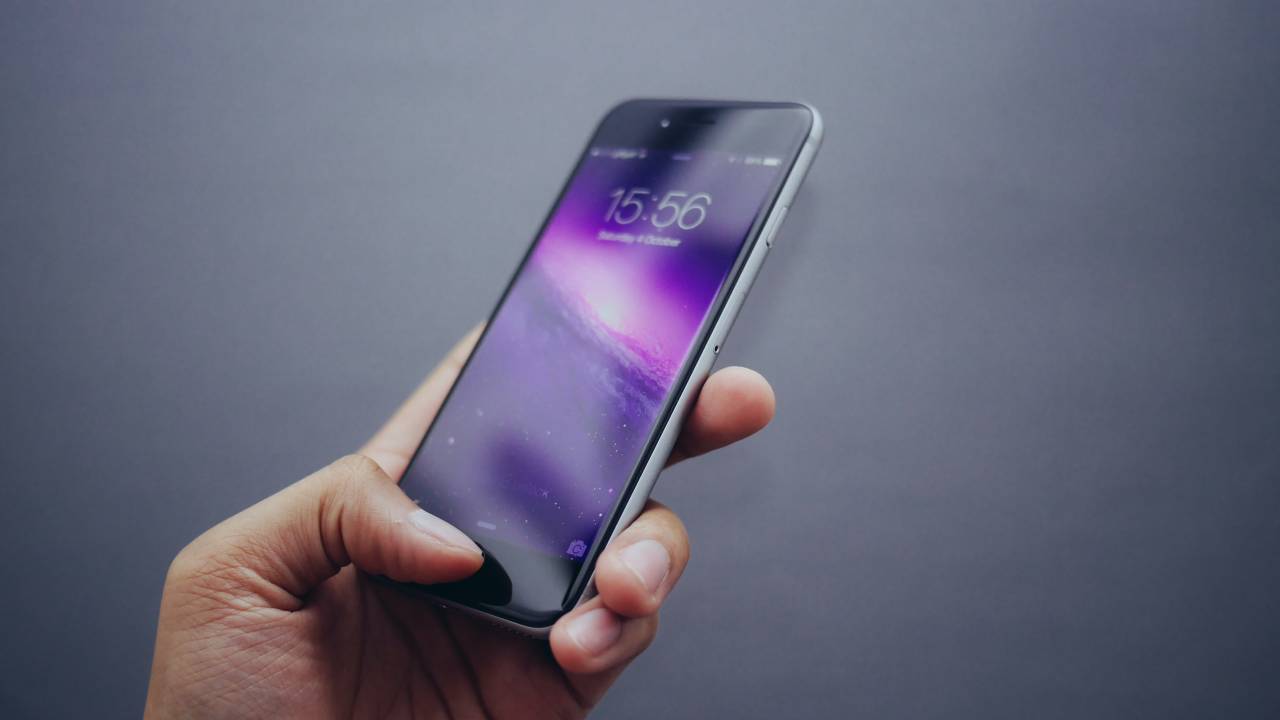 Foto de uma mão segurando um celular em que a tela está bloqueada
