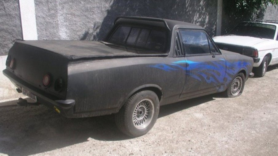 Imagem mostra um carro preto com chamas azuis pintadas nas laterais.