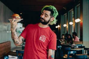Paulo Yoller com camiseta vermelha do Meats segurando um hambúrguer num prato.