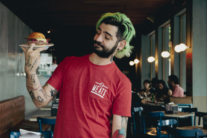 Paulo Yoller com camiseta vermelha do Meats segurando um hambúrguer num prato.