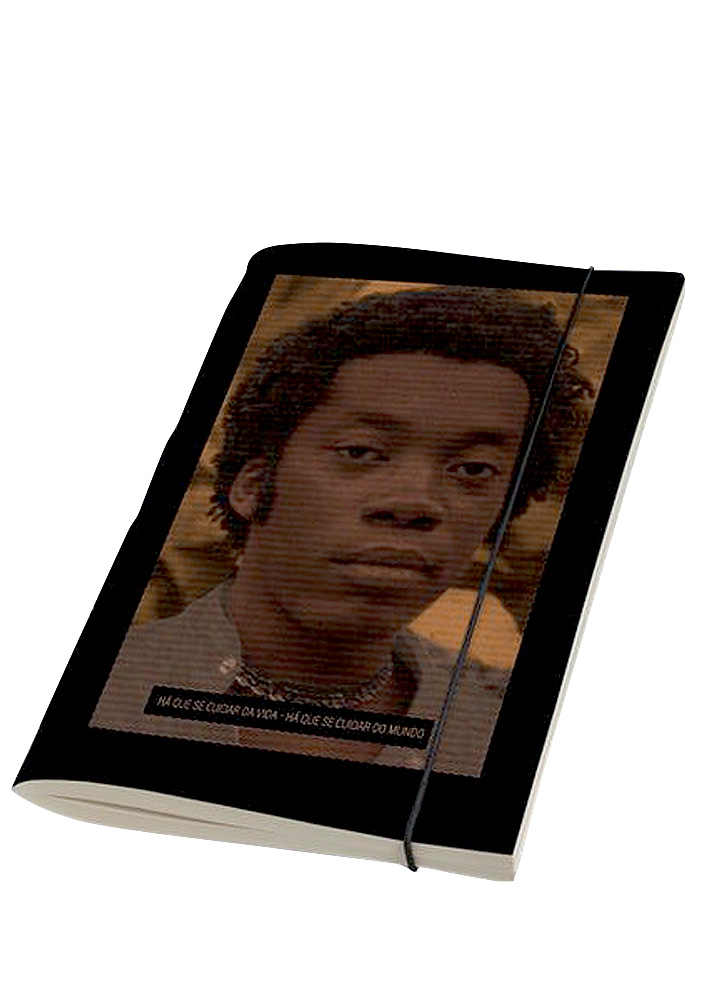 Um caderninho preto estampa a foto de um garoto negro. Está escurecida em tons de marrom