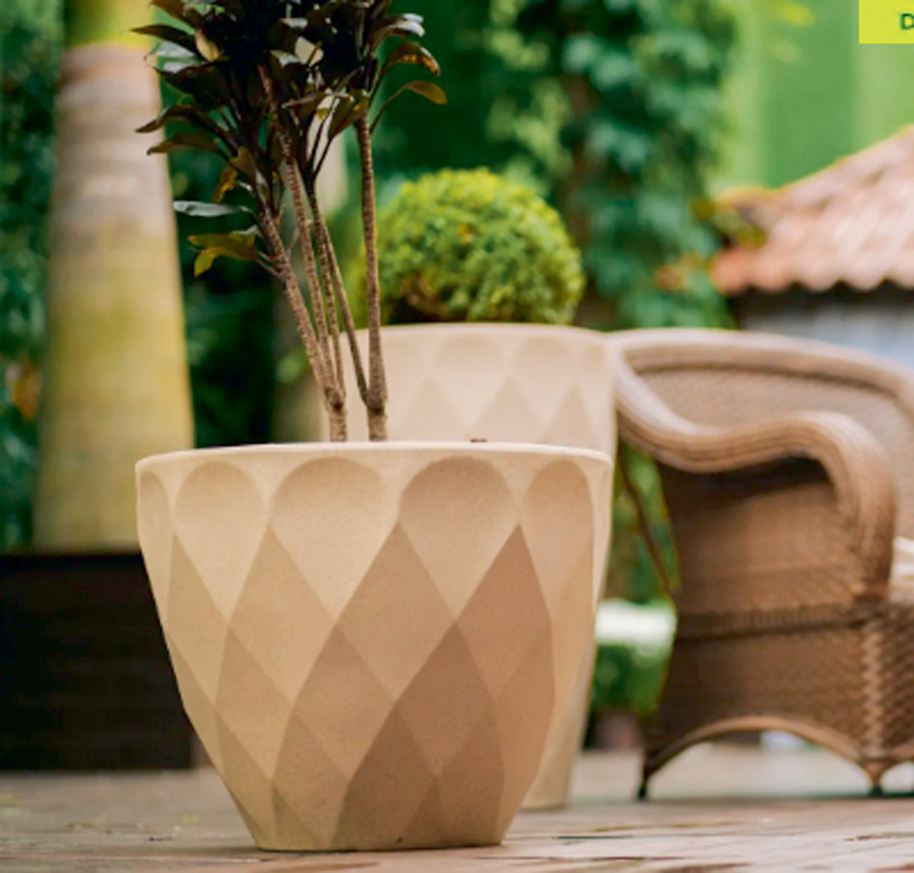 vaso.png Um vaso oval está no chão do que parece ser uma sala. Há móveis e outras plantas ao fundo