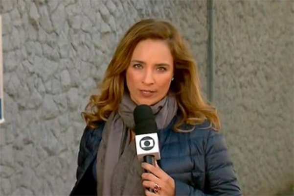 Imagem mostra Veruska usando cachecol e blusa, olhando para a câmera enquanto segura microfone da TV Globo