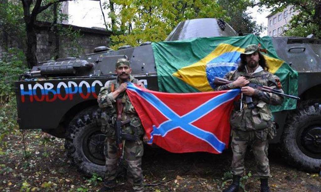 Imagem mostra Rafael, à direita, ao lado de um guerrilheiro e à frente de um tanque de guerra