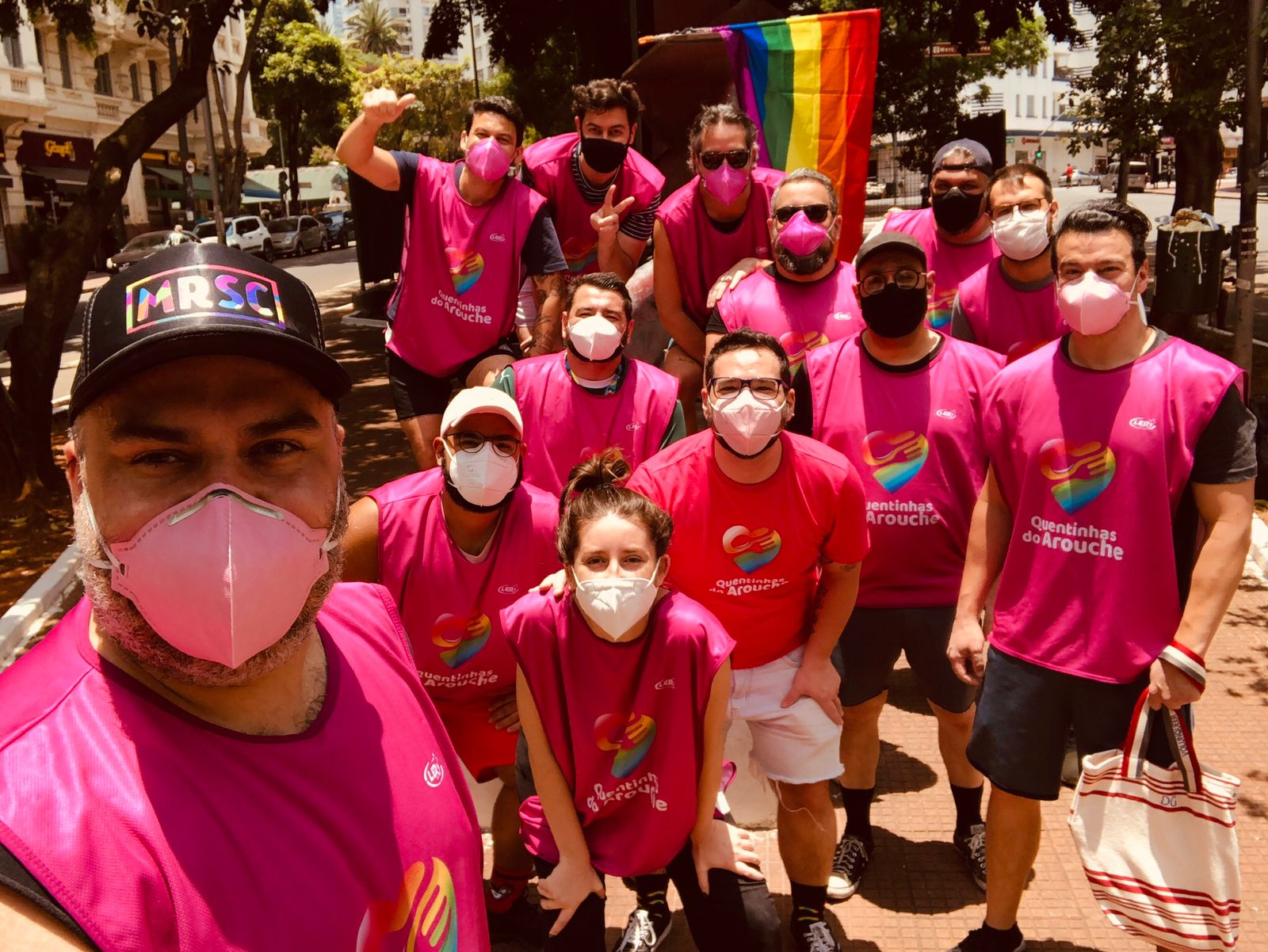 Voluntários do projeto tiram selfie. Eles trajam coletes cor-de-rosa e levam consigo uma bandeira LBGT.