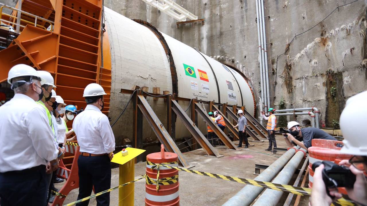 Imagem mostra Doria e assessores à esquerda e, ao fundo, enorme tuneladora, em formato cilíndrico. Eles estão no subsolo
