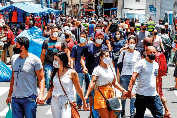 Imagem mostra multidão caminhando em rua. Todos usam máscara.
