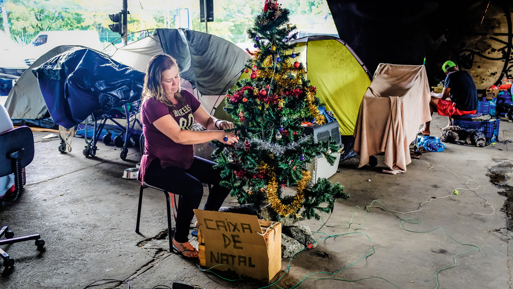 Imagem mostra mulher sentada em cadeira mexendo em árvore de Natal.