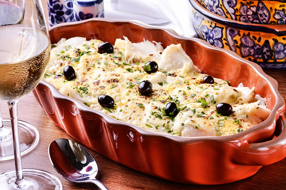 Bacalhau servido em cerâmica de cor marrom junto de azeitonas, batata e pequenas folhas verdes