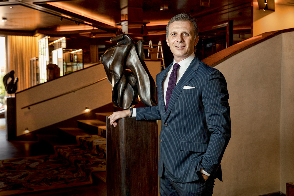 Um homem de terno posa em frente a uma escultura. Foto dentro de um hotel