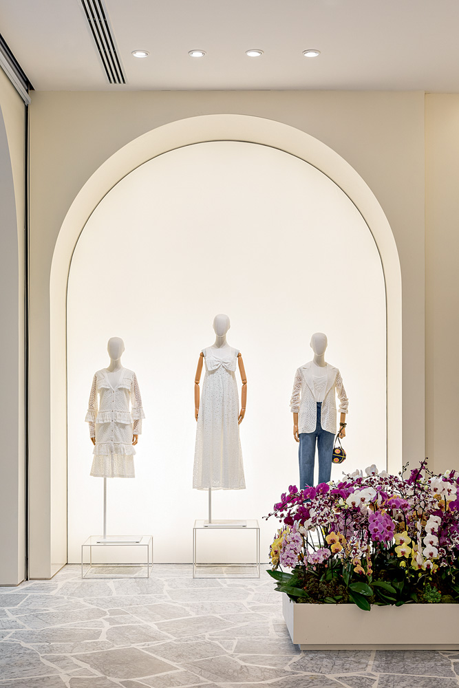 Foto mostra fachada de loja no shopping. Em um arco, há três manequins brancos vestidos