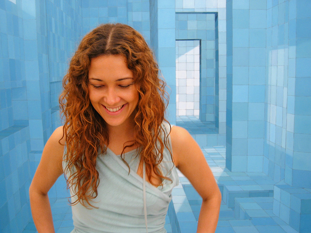 Imagem mostra mulher sorrindo com pintura geométrica azulada ao fundo.