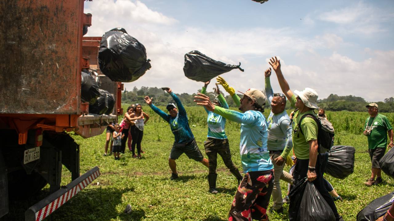 Imagem mostra um grupo de pessoas jogando sacos de lixo em um caminhão