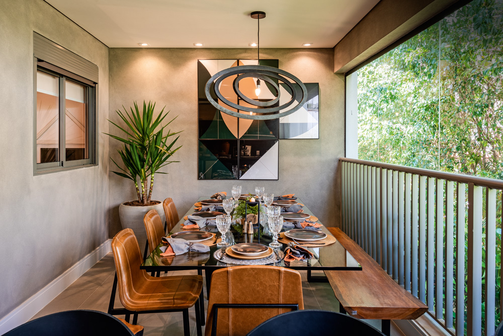 Decorado Tarjab Refuge – Setembro 2019-7.jpg Imagem mostra sala de jantar iluminada, com cadeiras bege, um banco de madeira, um quadro na parede e uma janela grande na lateral do cômodo.