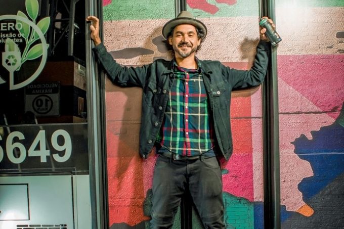 Artista posa com braços levantados pendurado na porta de um ônibus pintado