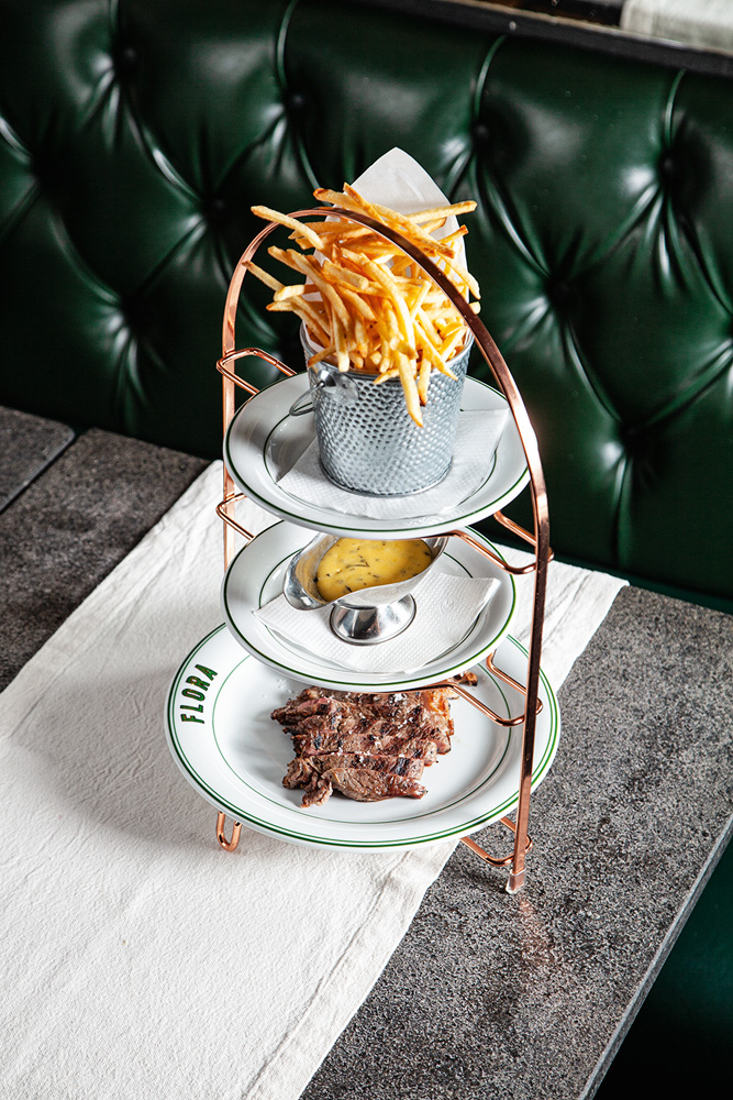 Filé de carne vermelha servida junto de uma porção de batatas fritas e molho amarelado em um suporte para três pratos