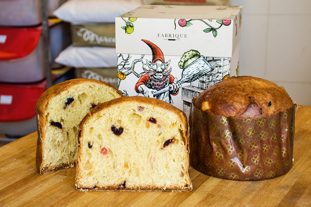 Fabrique Duas metades de um panetone e um panetone inteiro em frente a uma caixa decorada com tema natalino