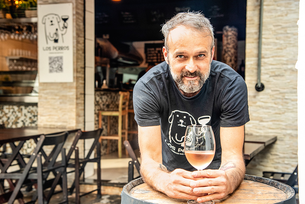 Fabiano Aurélio posa apoiado sobre uma mesa junto de uma taça de vinho