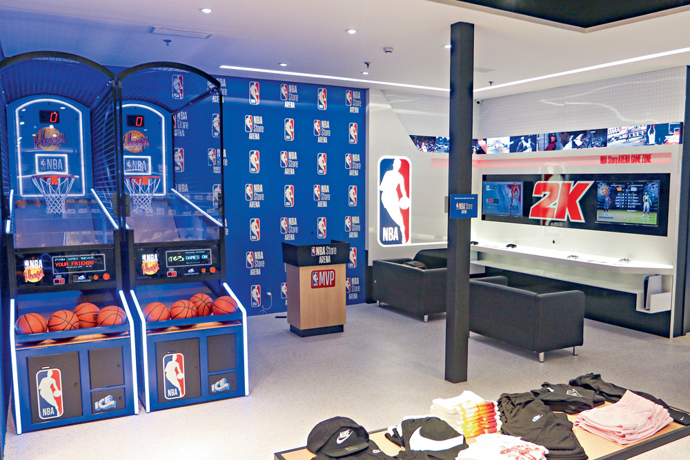 Foto mostra duas máquinas de brincar de cesta de basquete, alguns sofás e logos na NBA em paredes