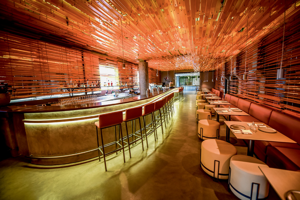 Foto mostra o salão do Priceless. Há um grande bar com banquetas e, do outro lado, mesas com poltronas. Ambiente alaranjado