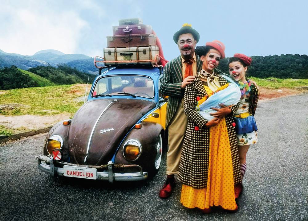 Cena de um filme mostra família de palhaços em uma estrada e na frente de um fusca, que está carregado de malas