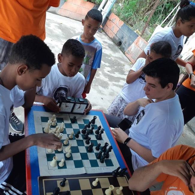 Foto mestra mestre internacional de xadrez Renato Quintiliano sentado disputando partida com crianças de projeto social em comunidade de Cotia, na Grande São Paulo