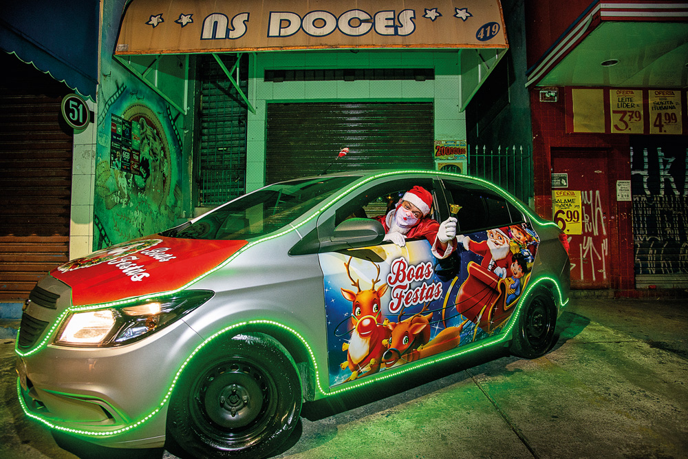 Imagem mostra carro com LEDs verdes e desenhos natalinos nas laterais. No banco de motorista, um homem vestido de papai noel.