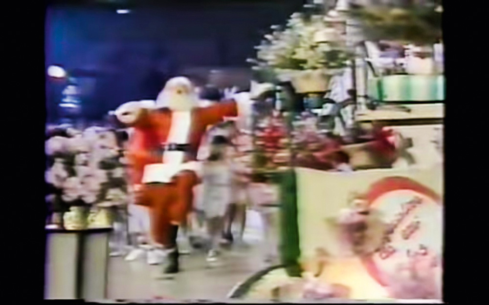 Imagem mostra frame de um comercial de Natal antigo, onde é possível ver um Papai Noel ao lado de decorações natalinas.