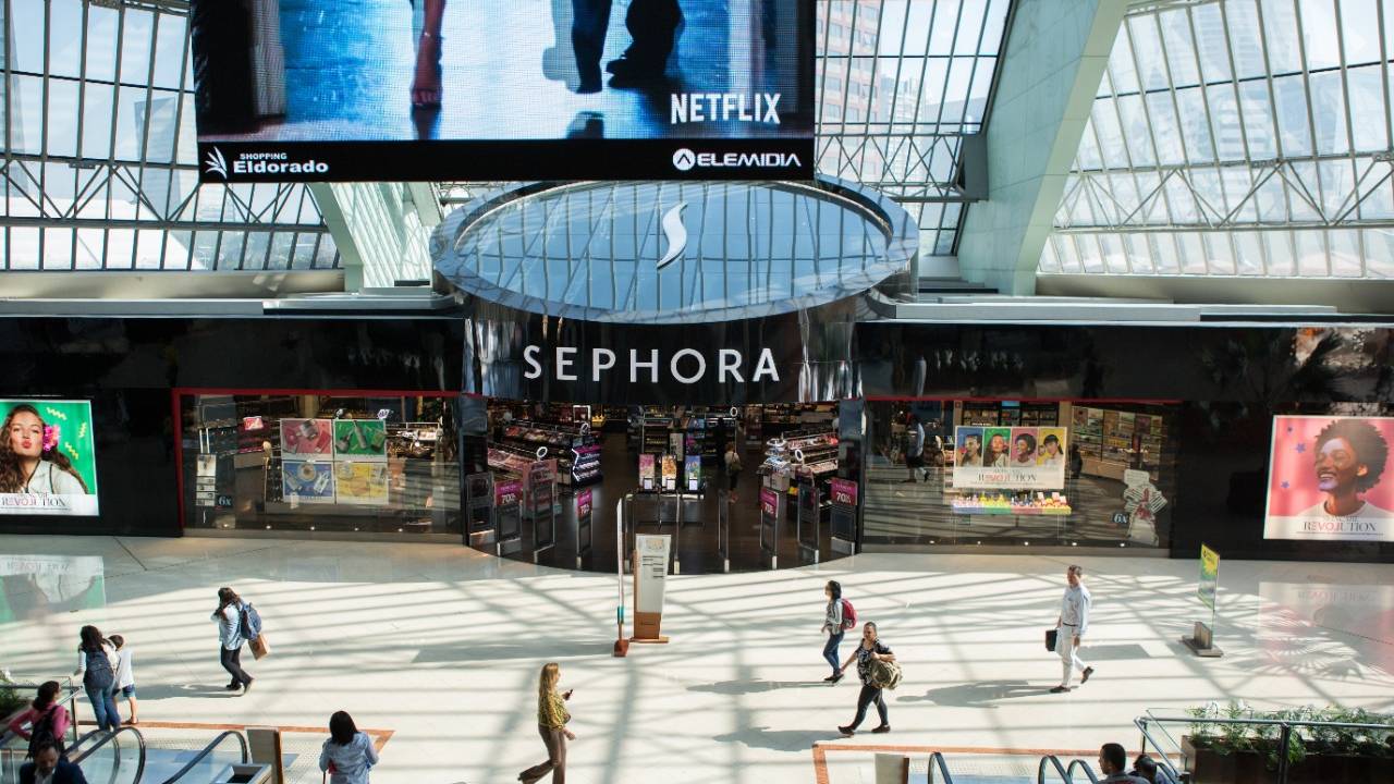 Foto mostra fachada da Sephora com pessoas passando em frente. No topo, grandes vidraças iluminam o shopping.