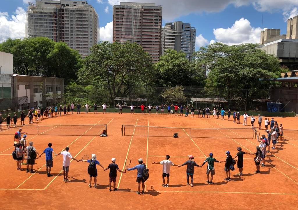 Imagem mostra tenistas amadores dando as mãos em volta de quadra de tênis do Complexo Mané Garrincha