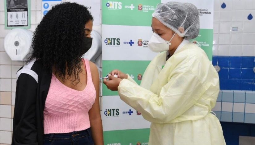 Profissional de saúde segura injeção e aplica vacina no braço de uma jovem